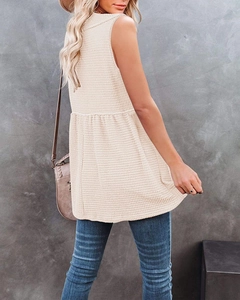 Detail view of beige waffle knit sleeveless top with ruffled hem and textured fabric