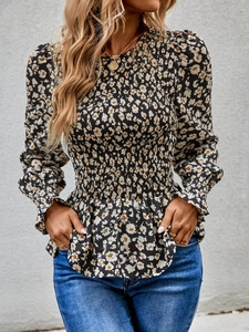 Detail of floral smocked blouse with high neck and ruffled hem against a gray wall