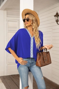 Detail of royal blue V-neck top with geometric embroidery trim and batwing sleeves