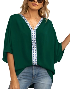 Detail of V-neckline featuring blue and white geometric embroidery on dark green blouse