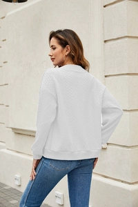 Close-up of white waffle knit sweater with cable stitching and ribbed texture details