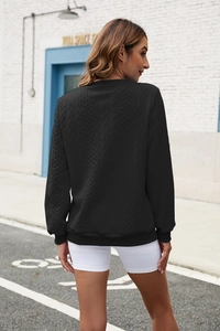Detail of black cable knit sweatshirt showing intricate 3D texture and ribbed cuffs