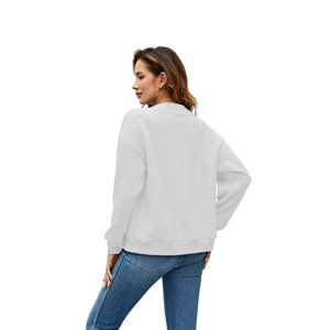 Detail of white long sleeve top with textured diamond pattern and ribbed cuffs on model