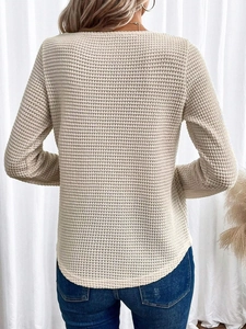 Dettaglio della trama a nido d'ape e bordo curvo sulla maglia beige a maniche lunghe da donna