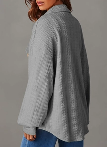 Dettaglio della camicia grigia a maniche lunghe con texture a pieghe e bottone dorato