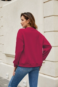 Macro detail of dark rose red knit sweater showing cable stitch texture and ribbed cuffs