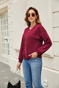 Close-up of wine red knitted jacket featuring silver zipper and classic cable knit pattern