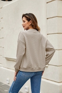Detailed cable knit texture of beige long sleeve sweater with ribbed cuffs and hemline