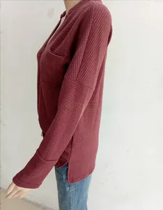 Detail of burgundy waffle knit texture and side slit hem on a loose V-neck top