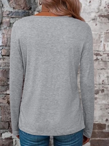 Back view of a light grey long-sleeve knit T-shirt worn against a red brick wall