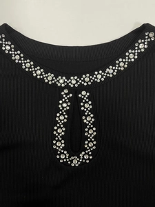 Detail of black ribbed knit top featuring a round neckline with rhinestone embellishments