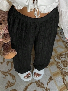 Detail of black high-waisted trousers featuring vertical openwork embroidery texture
