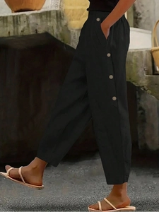 Detail of loose fit black casual trousers with button decor and elastic high waist