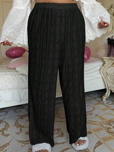 Detail of black high-waisted wide-leg trousers featuring a unique hollow-out crochet texture