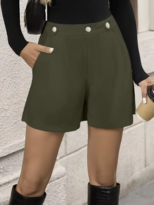 Detail of dark green corduroy shorts with high waist, pleated texture and silver buttons