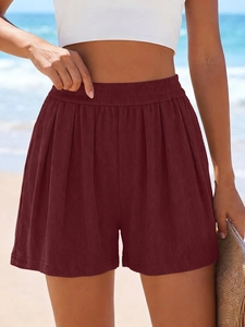 Détail du short en maille bordeaux taille haute avec ceinture élastique sur fond de plage