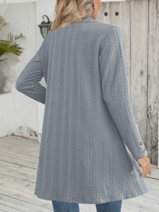 Detail eines blaugrauen Strick-Cardigans mit Zopfmuster und Goldknöpfen an den Bündchen