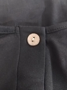 Detail showing the light-colored button and stitching on black cotton blend fabric