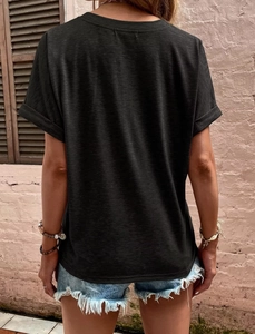 Back view of a black short-sleeved t-shirt with folded cuffs against a pink wall