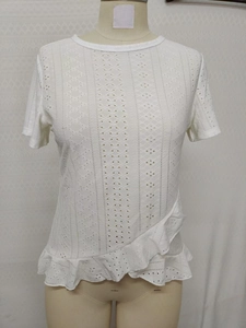Detailed view of white short-sleeve top with floral eyelet embroidery and ruffle hemline