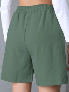 Detail view of high-waisted dark green linen shorts with elastic waist and pocket