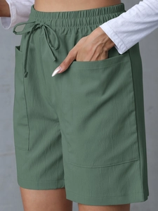 Detail of dark green linen shorts with elastic drawstring waist and large front pockets