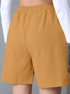 Detail view of ginger yellow linen shorts with elastic ruched waistband and textured fabric
