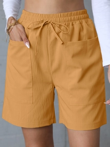 Detail of high-waisted linen shorts in ginger yellow with elastic drawstring and large pockets