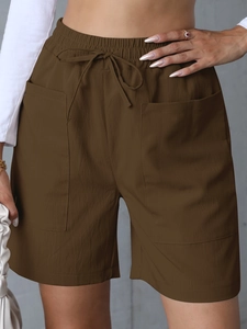 Detail of high-waisted linen shorts featuring large square pockets and drawstring waist