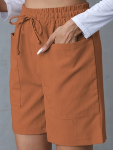 Detail of high-waisted brick red linen shorts with elastic drawstring and large pockets