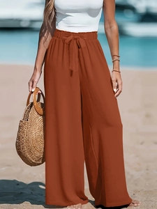 Dettaglio dei pantaloni larghi a vita alta caramello con fiocco e texture lino