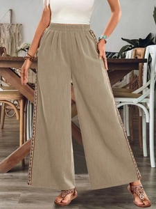 Detail der High-Waist-Hose mit weitem Bein und bunter geometrischer Stickerei an der Naht