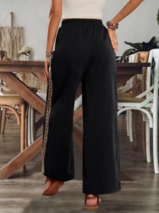 Detail einer schwarzen Weitbeinhose mit hoher Taille und farbigem Ethno-Stickerei-Besatz