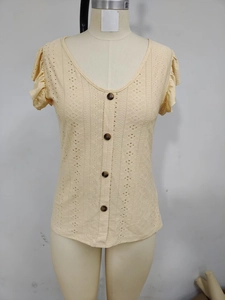 Detail of light yellow eyelet embroidery fabric with dark brown buttons and a deep V-neckline