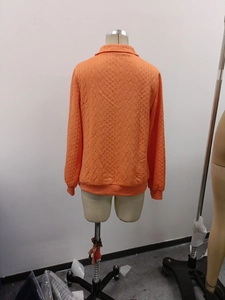 Detailed back view of bright orange knit sweater showing intricate 3D cable stitch pattern