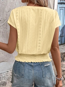 Detail of light yellow smocked blouse showing floral eyelet embroidery and elastic hem