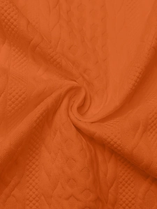 Macro shot of vibrant orange knitted fabric with intricate diamond pattern textures