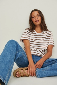 Detail eines gestreiften Kurzarm-T-Shirts mit blauer Jeans und gewebten Sandalen im Sommerstil