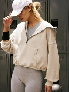 Detail of beige half-zip hoodie featuring a front pocket and ribbed cuffs in gym setting