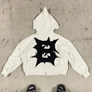 Flat lay of white heavy cotton hoodie featuring a large black spiked B embroidery on the back