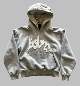 Detailansicht eines grauen Kapuzenpullovers mit weißer Buchstabenstickerei im Streetwear-Stil