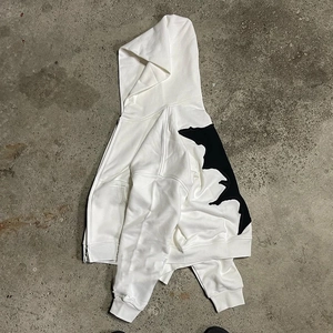 Detail of white zip hoodie featuring black jagged patchwork and heavy cotton fabric texture