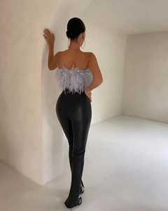 Dettaglio del top grigio con piume e zip e dei pantaloni neri in ecopelle con spacco