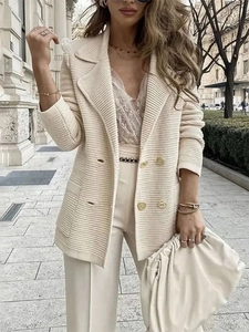 Detail van een gebroken witte ribgebreide blazer met gouden knopen en grote revers
