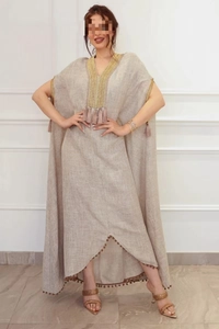 Détail d'un caftan en lin avec broderie dorée et pompons rose pâle sur l'encolure