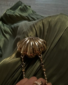 Detailed close-up of golden shell evening clutch with metallic chain on green fabric