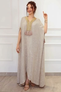 Détail d'une robe caftan en lin gris avec broderies dorées et pompons roses sur le col en V
