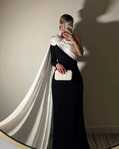 Detail van elegante zwarte avondjurk met witte 3D-roos en gedrapeerde cape-stijl