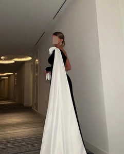 Detail van de grote witte zijden bloem en elegante lange cape op een zwarte avondjurk
