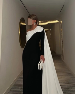 Detail van zwarte jurk met grote witte 3D-bloem en een elegante lange cape